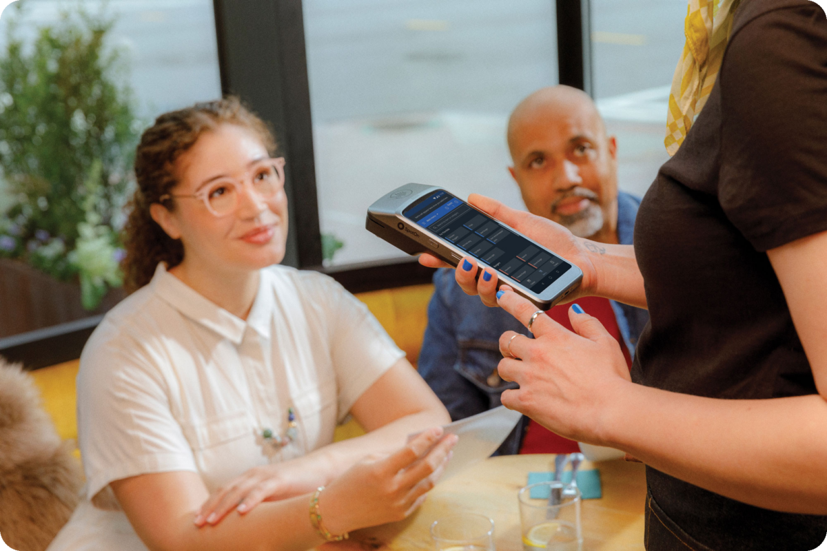 Female waiter using the Oracle Simphony handheld POS to check out a table